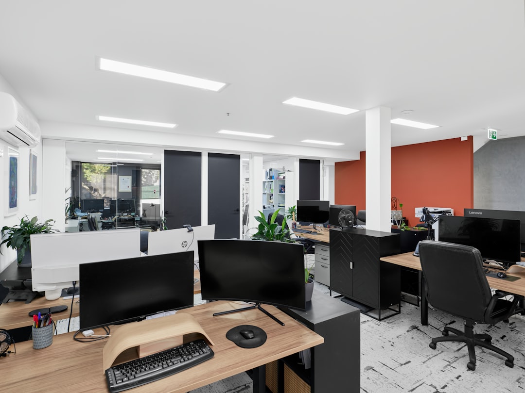 An empty open-plan office with rows of desks, widescreen monitors and task chairs